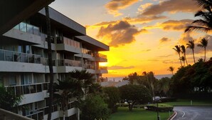 A modern building with multiple balconies overlooking a well-maintained garden and a curved road. - PRICES SLASHED!! Partial Ocean View + Short Walk to Everywhere You Want to Go (kihei)