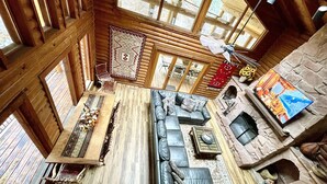 Un interior de cabaña espacioso con una gran mesa de comedor de madera, un sofá de cuero y una chimenea de piedra.