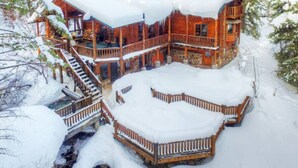 Una cabaña de troncos con una terraza de madera y varios balcones, rodeada de árboles cubiertos de nieve.