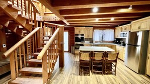 Una escalera de madera que conduce a una cocina con comedor, armarios de madera y un refrigerador de acero inoxidable.