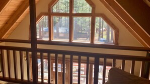 Una habitación con barandilla de madera en el balcón, un ventanal de varios paneles y vistas a un área boscosa.