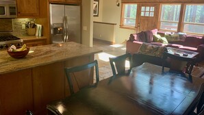Una cocina con armarios de madera, encimera de granito y refrigerador. Hay una zona de comedor con mesa y sillas.