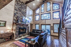 A spacious living room with a stone fireplace, leather sofa, and large windows.