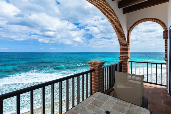 A balcony with a view of the ocean, featuring brick arches and a tiled floor.