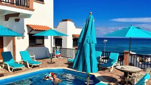 Un área de piscina con sillas de descanso y sombrillas, una piscina pequeña y vistas al océano.