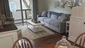 A cozy living room with a dining table, a sofa, and a ceiling fan. - Updated poolside villa, short walk to beach and Coligny Plaza (Hilton Head Island)