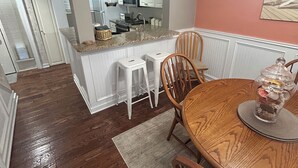 A dining area with a wooden table and chairs, a kitchen in the background, and a painting on the wall. - Updated poolside villa, short walk to beach and Coligny Plaza (Hilton Head Island)