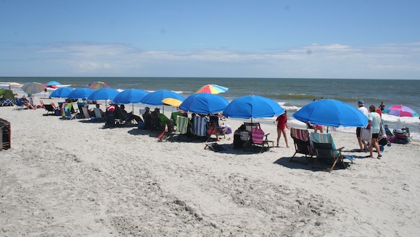 A beach with rows of beach chairs and umbrellas, some with colorful canopies, under a clear sky. - Updated poolside villa, short walk to beach and Coligny Plaza (Hilton Head Island)