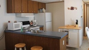 Eine kompakte Küche mit Holzschränken, einem weißen Kühlschrank, einer Mikrowelle und einer kleinen Kücheninsel mit Hockern.