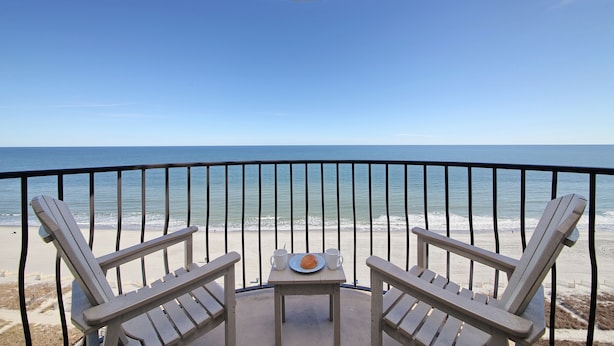 A balcony with two Adirondack chairs and a small table with a plate and two cups. The view includes a beach and the ocean. - +Serenity by the Sea+, Family Friendly, Best Views/ Location, Direct OF Corner! (Myrtle Beach)