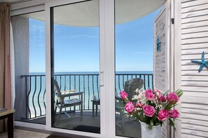 Enjoy ocean views from this balcony, featuring a glass door, wooden chair, and small table for relaxation or dining.