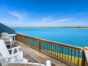 A wooden deck with white chairs and a table overlooking a body of water.