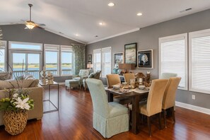 A spacious living room with a dining area, large windows with blinds, a ceiling fan, and a view of the outdoors.
