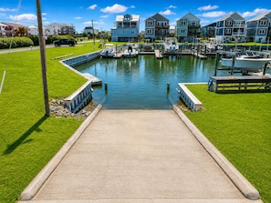 A marina with boats docked, a concrete walkway leading to the water, and residential buildings in the background. - Best Views On The Island! Ocean, waterfront, Boat Dock, Elevator, Pool, Fish! (Topsail Beach)