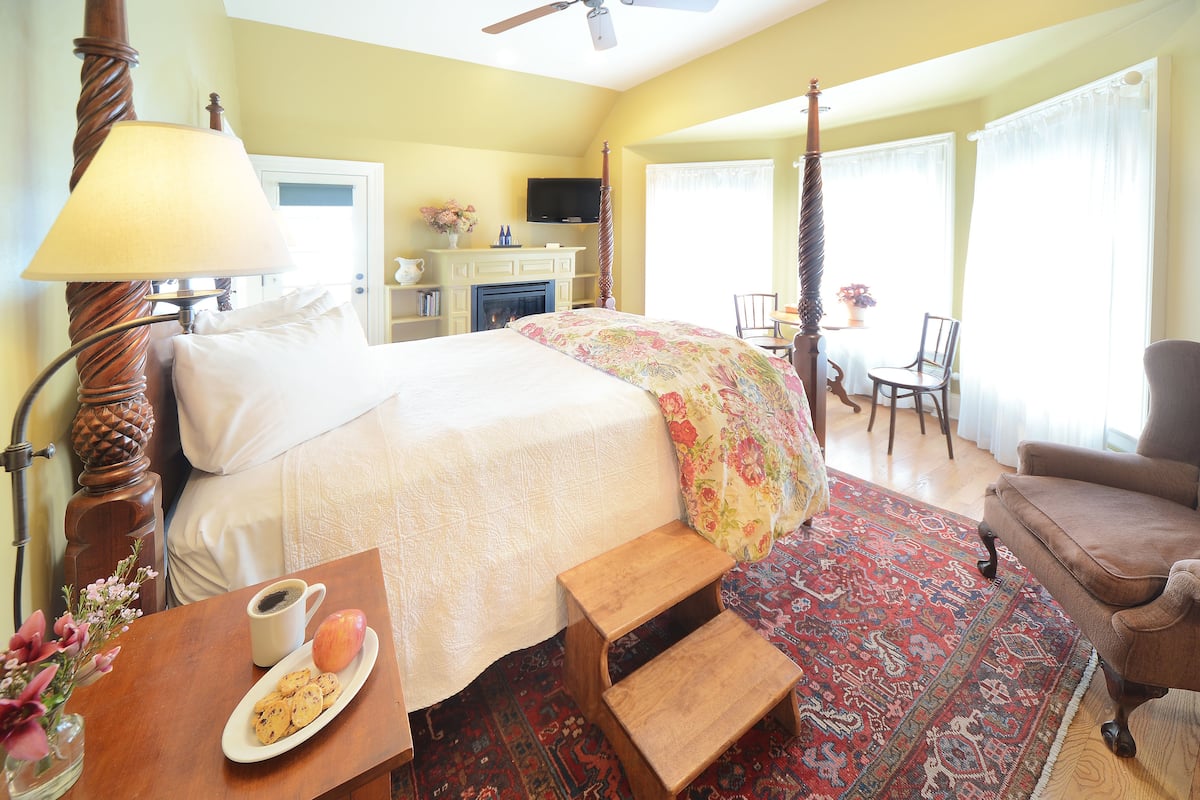 A hotel room with a bed, a wooden chair, a small table with a cup and cookies, and a television on the wall.