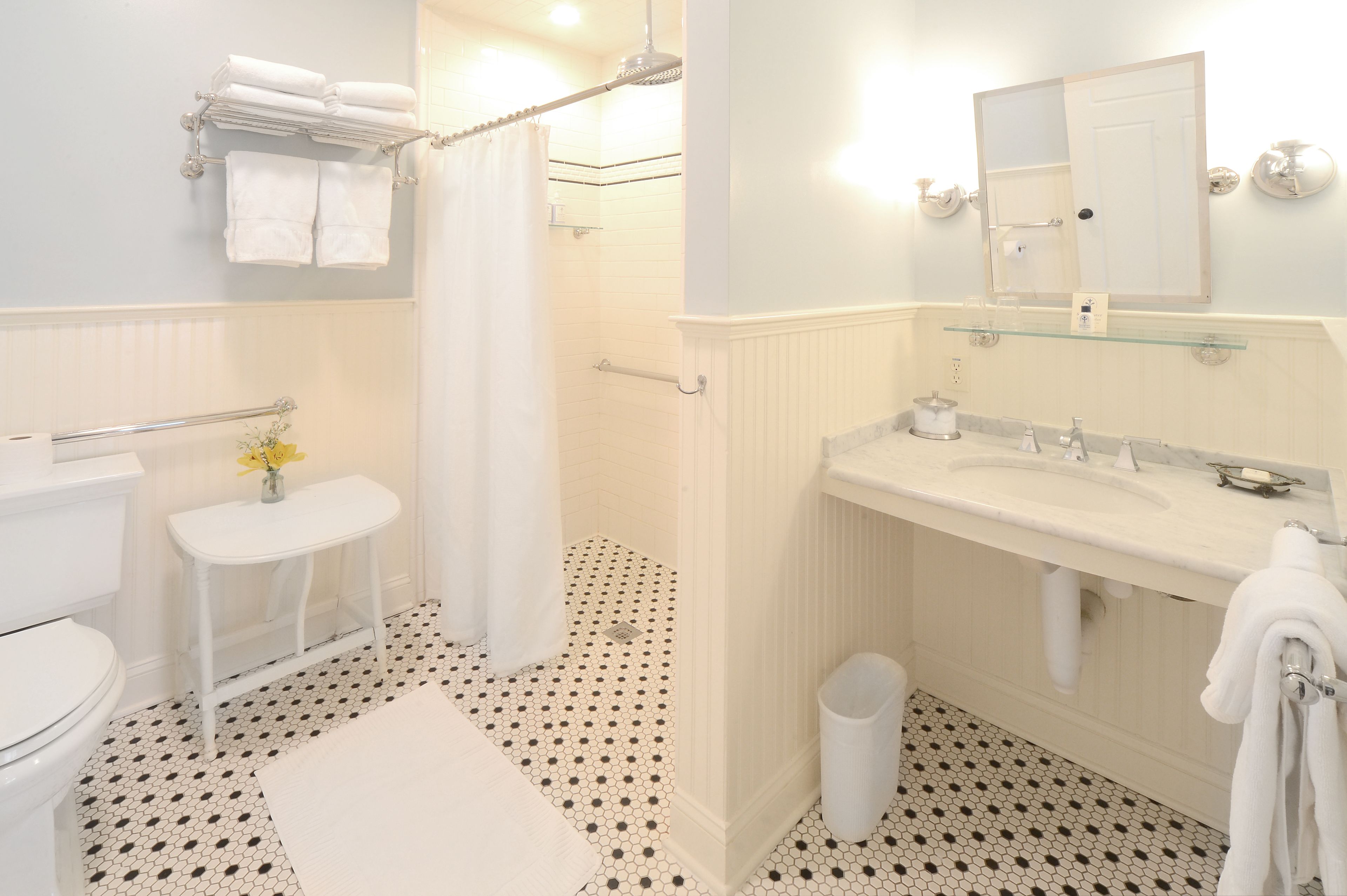 A bathroom with a toilet, sink, shower, and a glass shelf above the sink.