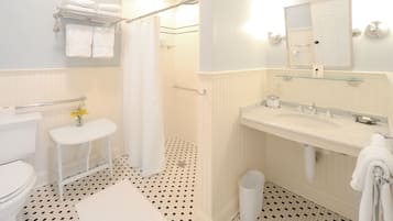 A bathroom with a toilet, sink, shower, and a glass shelf above the sink.