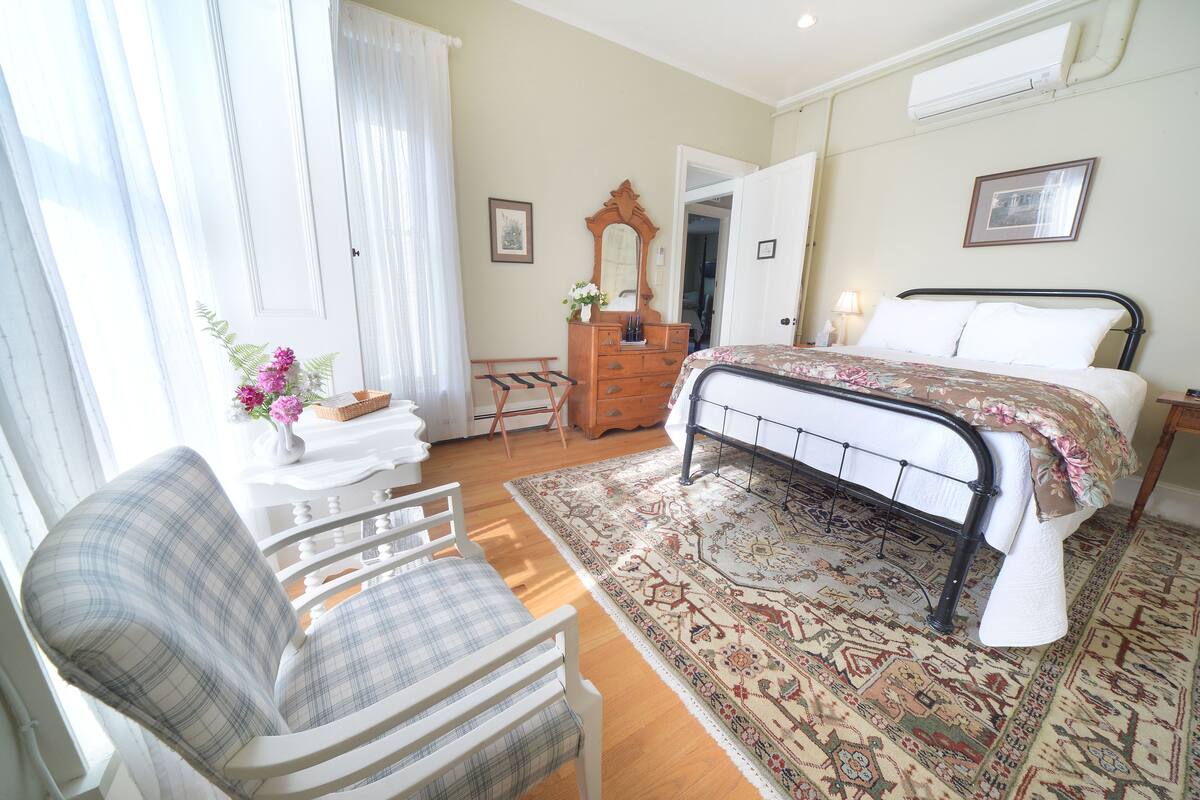 A bedroom with a bed, a chair, a dresser, and a mirror.