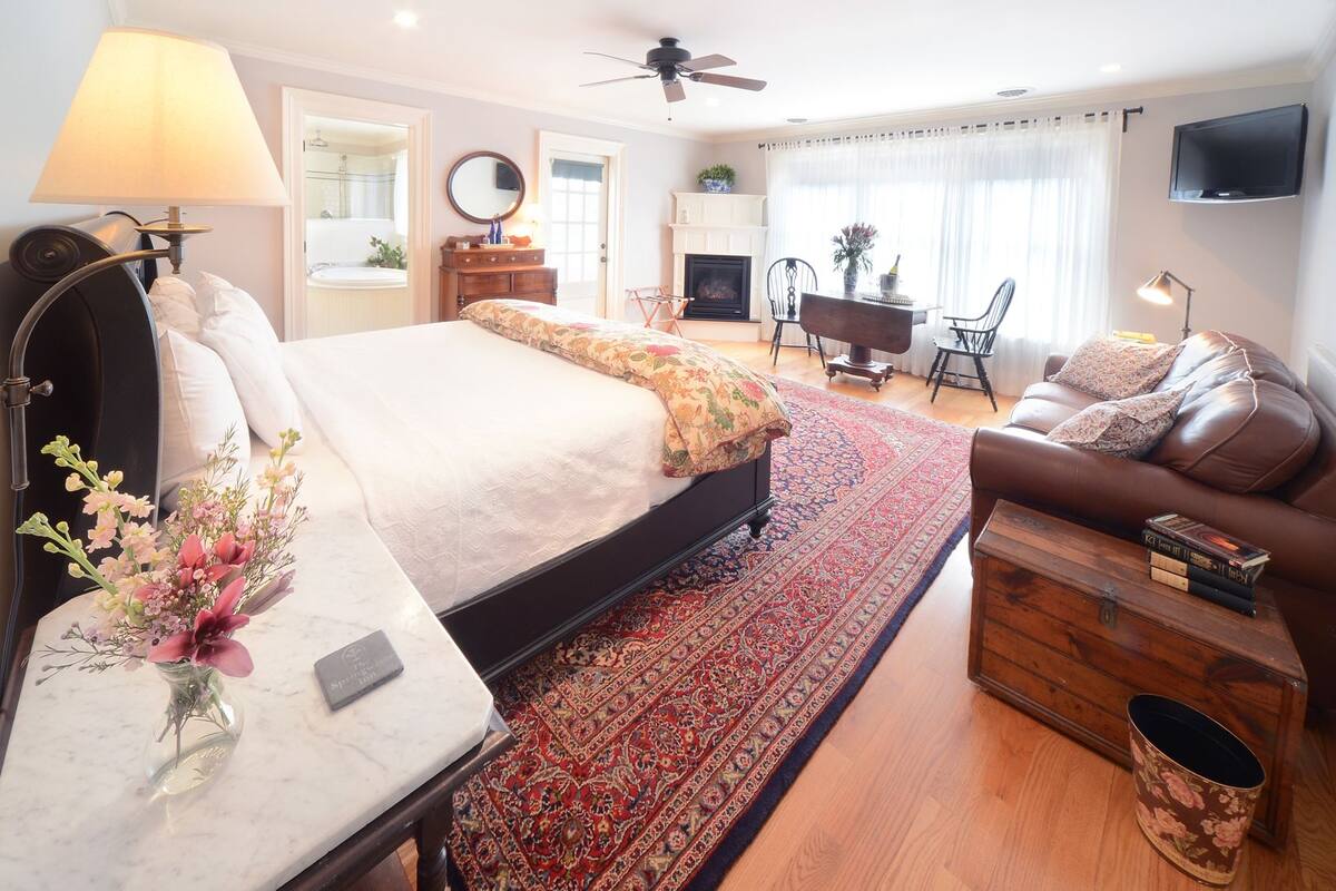 A hotel room with a bed, a sofa, a TV, a fireplace, and a dining area.