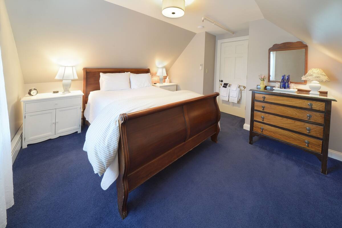 A bedroom with a large wooden bed, a dresser with drawers, a nightstand with a lamp, and a mirror above the dresser.