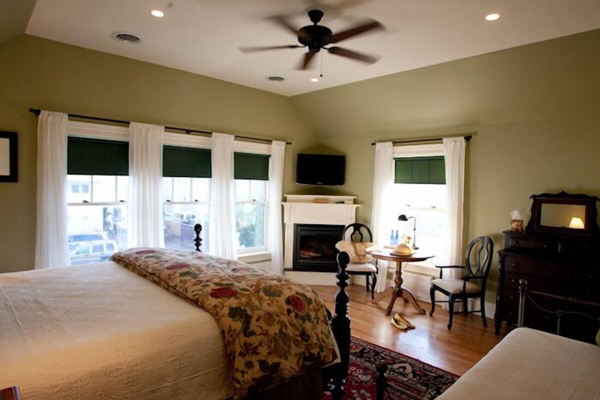 A bedroom with a bed, a fireplace, a television, and a ceiling fan.