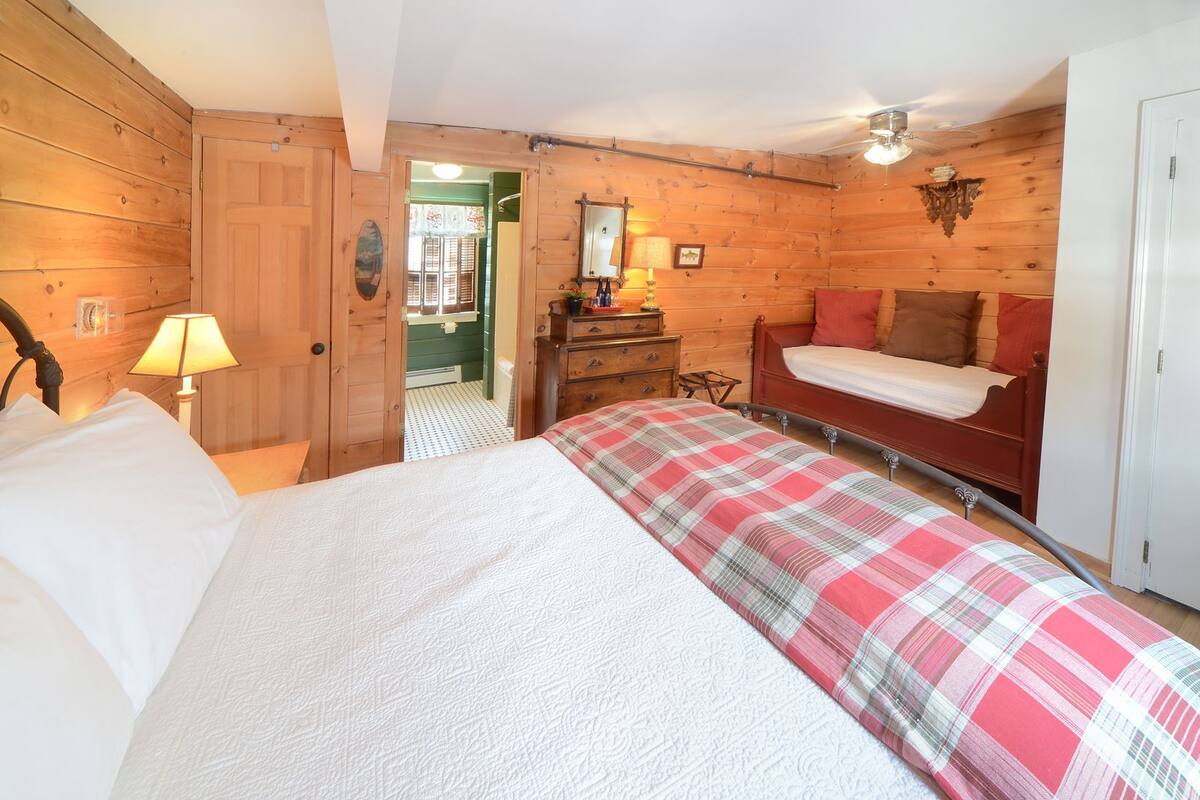 A wooden room with a bed, a dresser, a mirror, and a door.