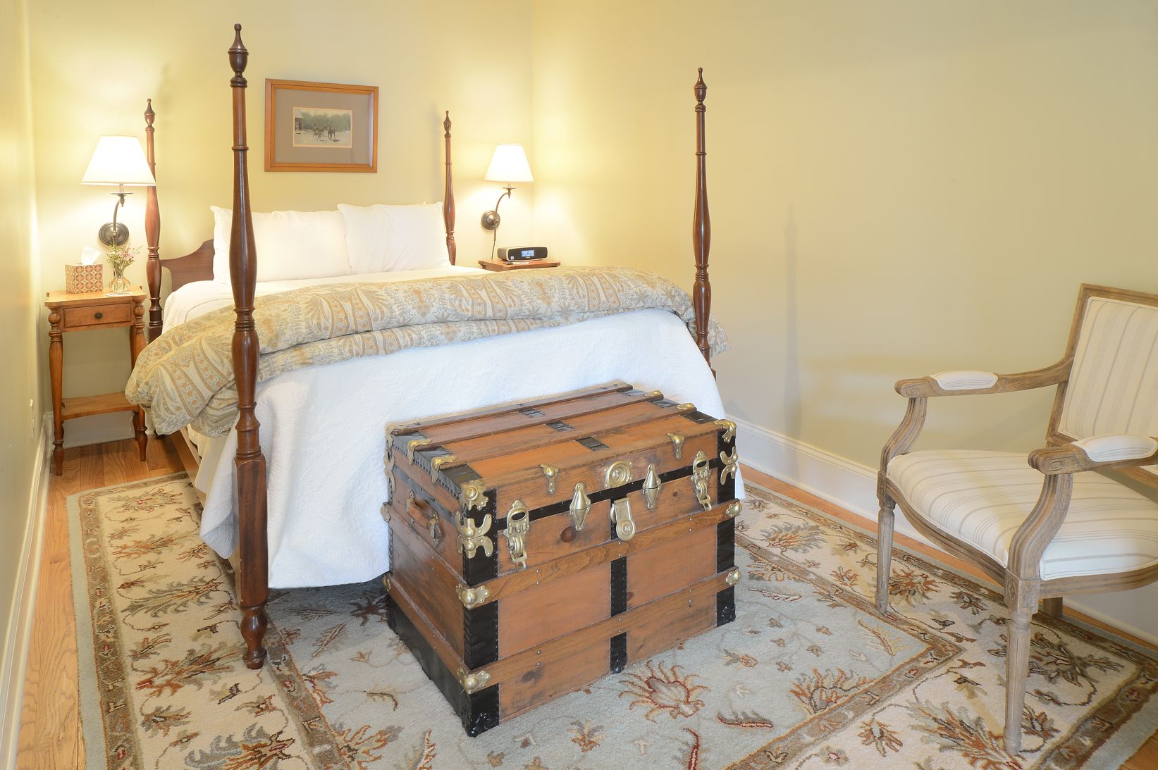Una cama con dosel, un aparador de madera, una silla y dos mesitas de noche con lámparas.