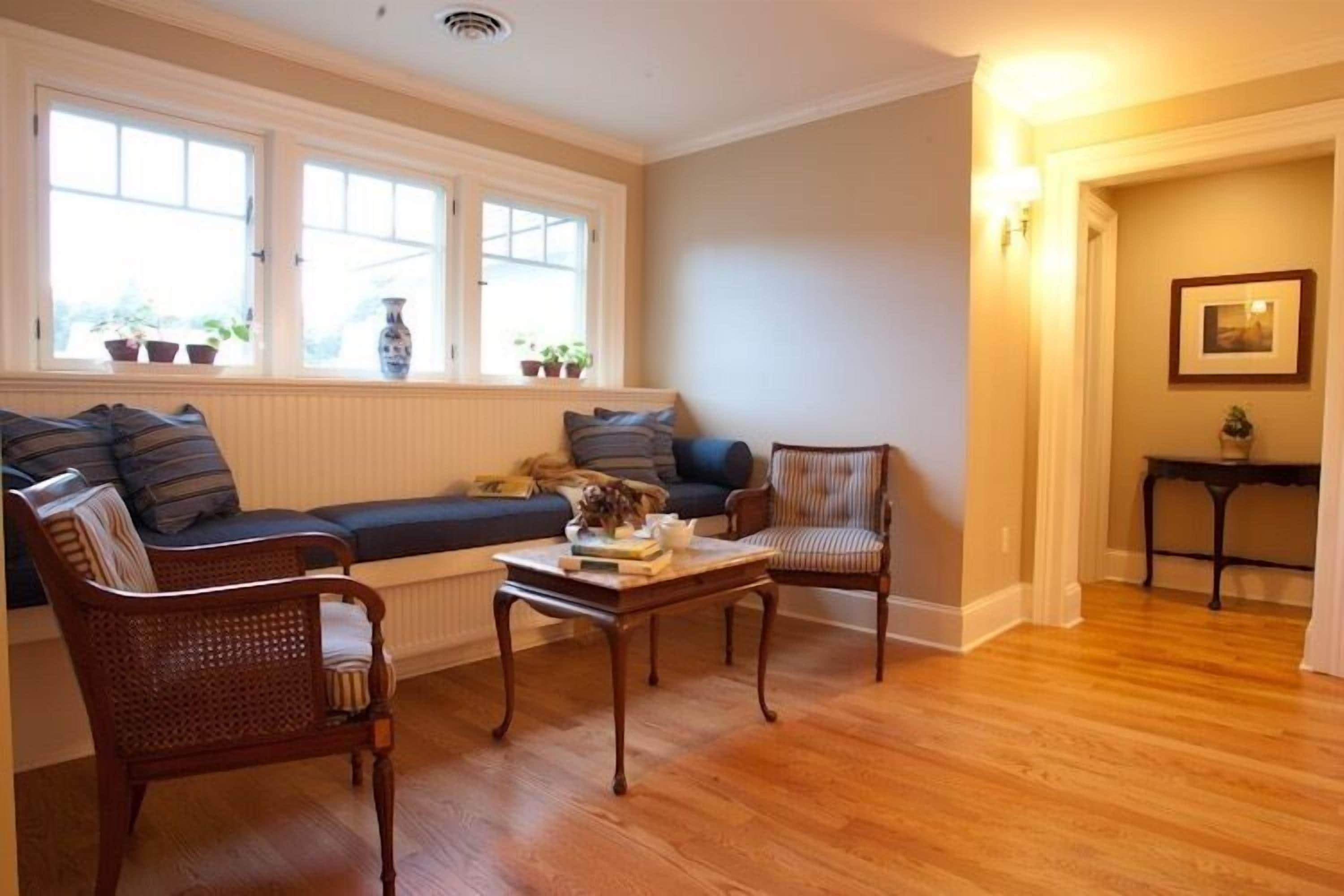Una sala de estar acogedora con un sofá, dos sillones, una mesita de centro y una ventana con plantas.
