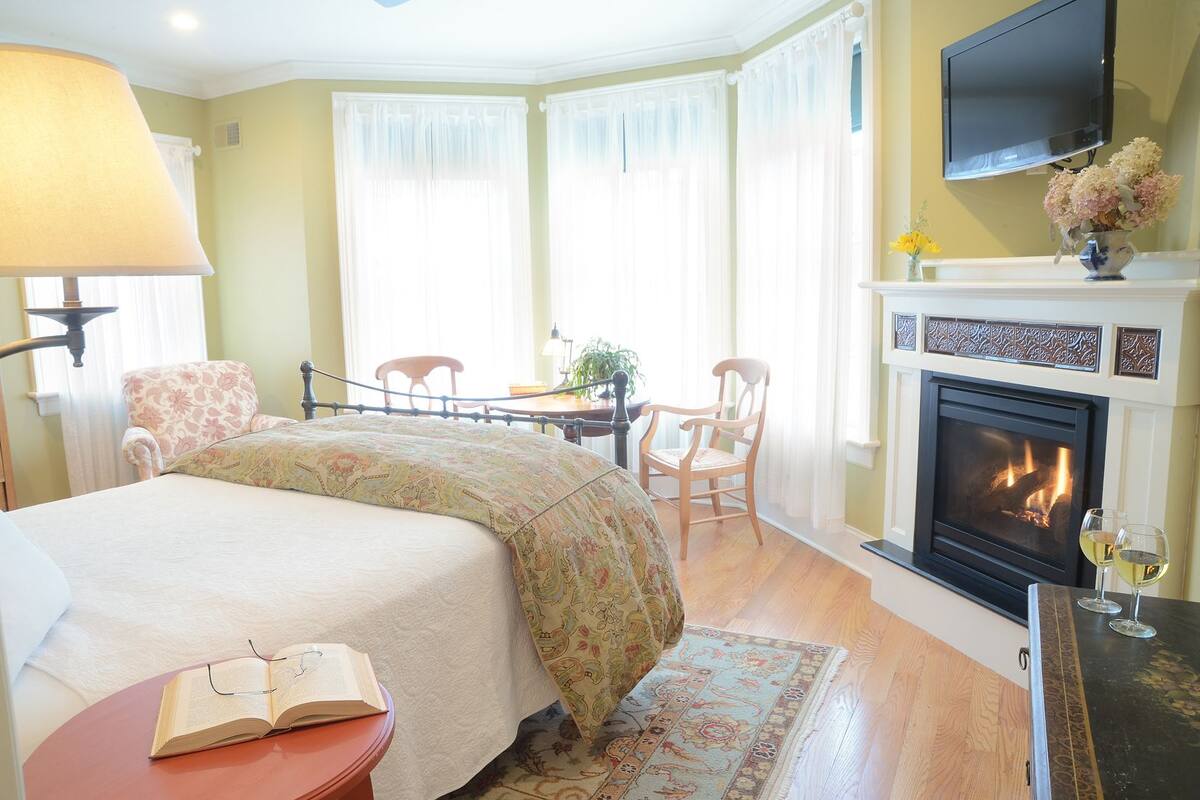 A hotel room with a bed, a desk, a chair, a fireplace, and a TV.