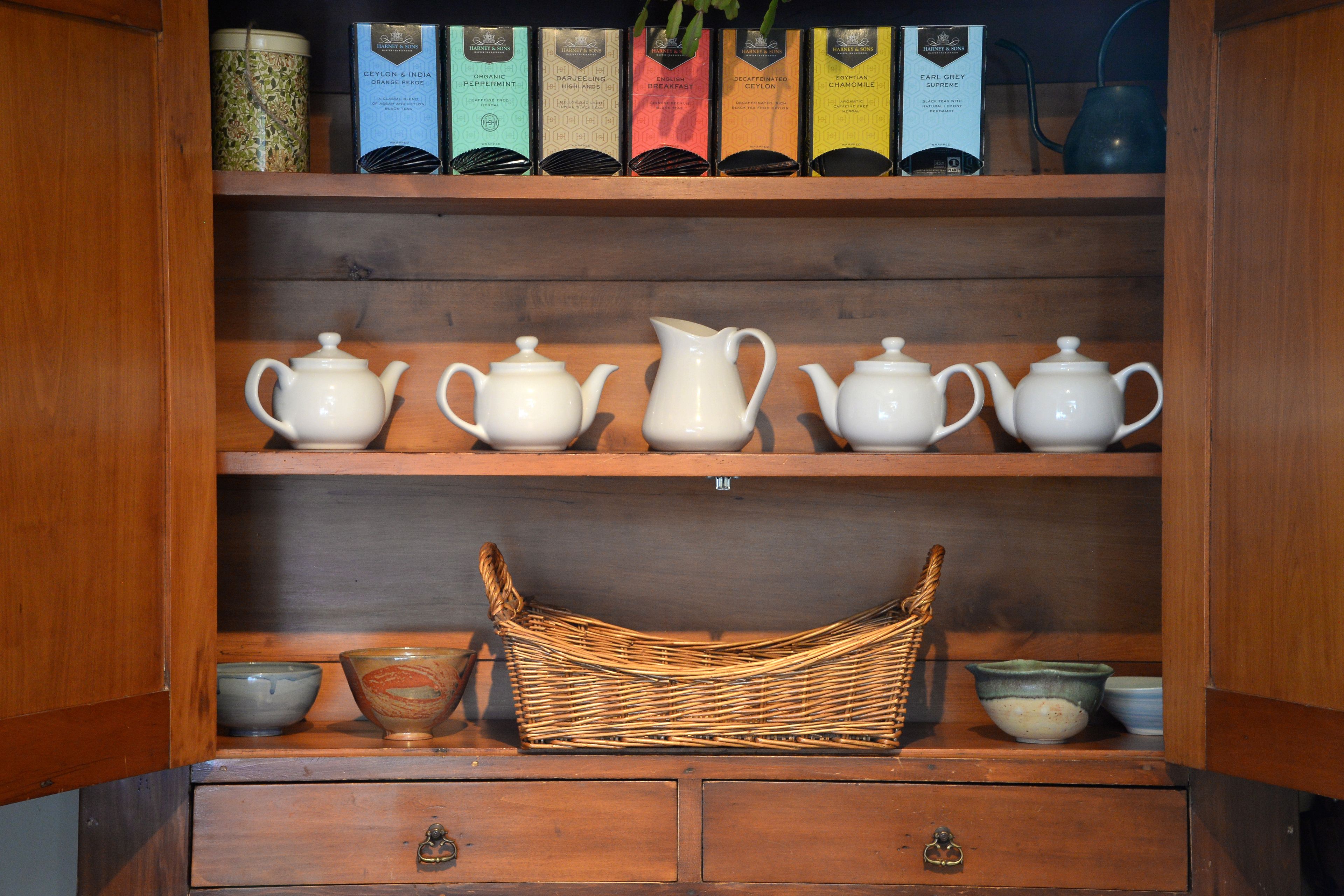 A wooden cabinet with shelves holding tea boxes, teapots, and a wicker basket.