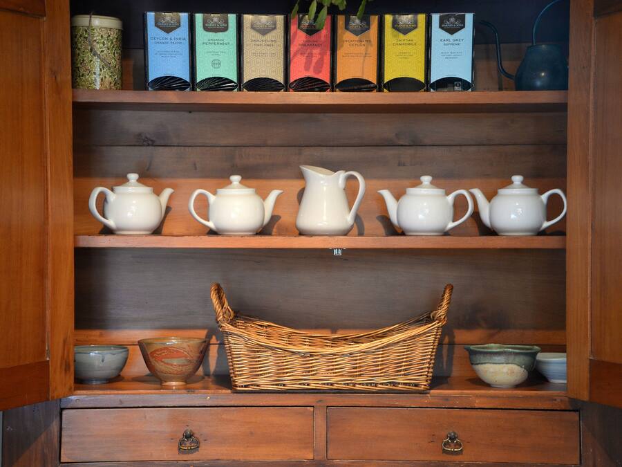 A wooden cabinet with shelves holding tea boxes, teapots, and a wicker basket.
