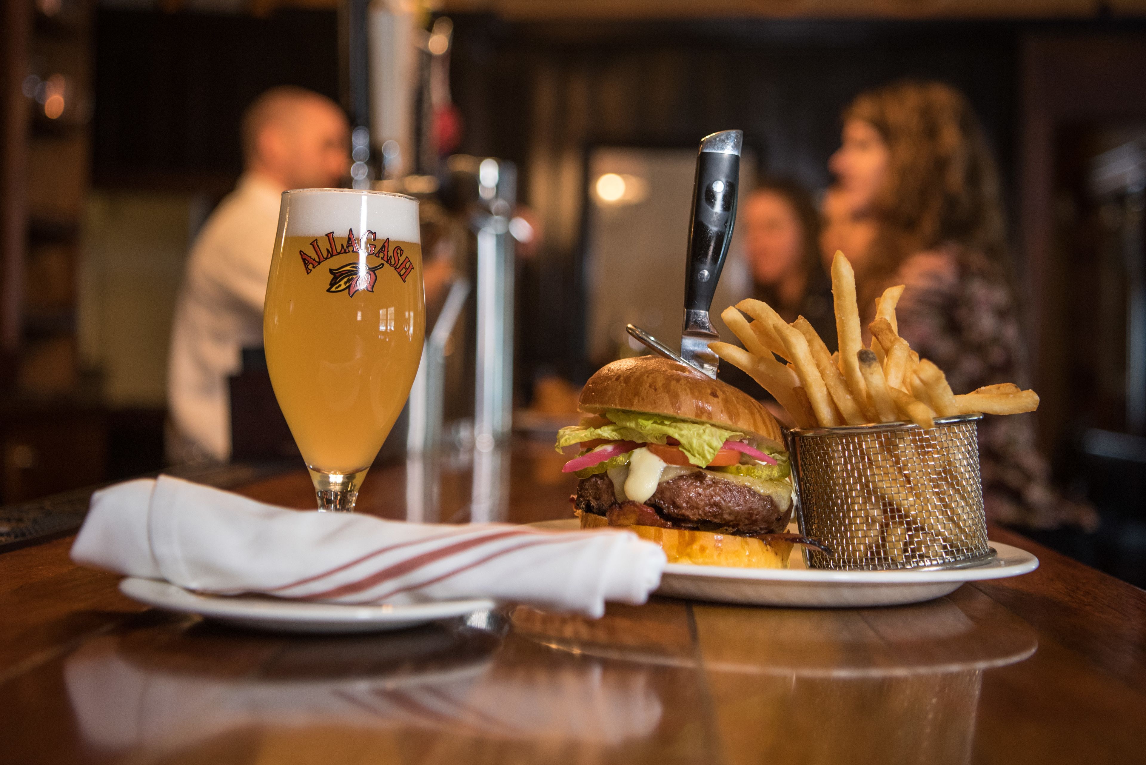 A meal with a burger, fries, and a glass of beer on a wooden table.
