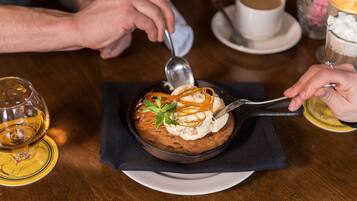 A dessert in a bowl with a spoon, a cup of coffee, and a glass of wine on a table.