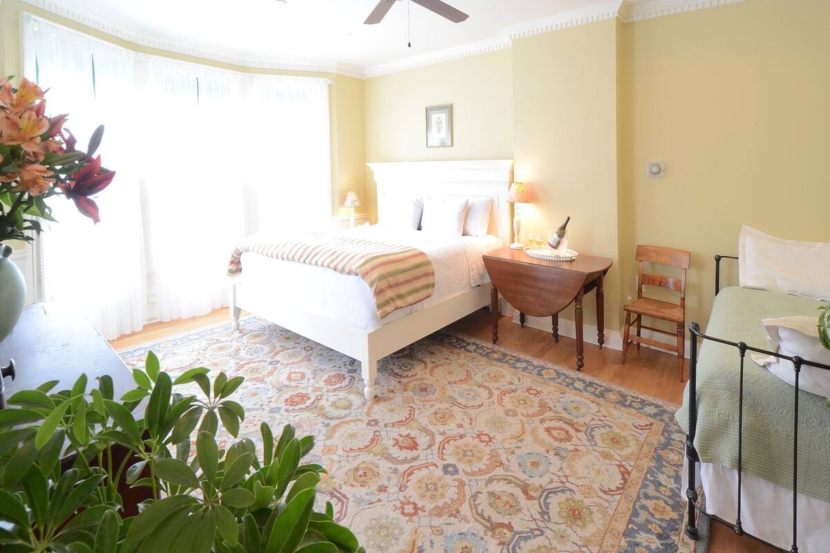 A bedroom with a bed, bedside table, chair, and a large window with curtains.