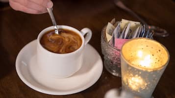 A cup of coffee on a saucer with a spoon, a glass candle holder, and a glass with a candle.