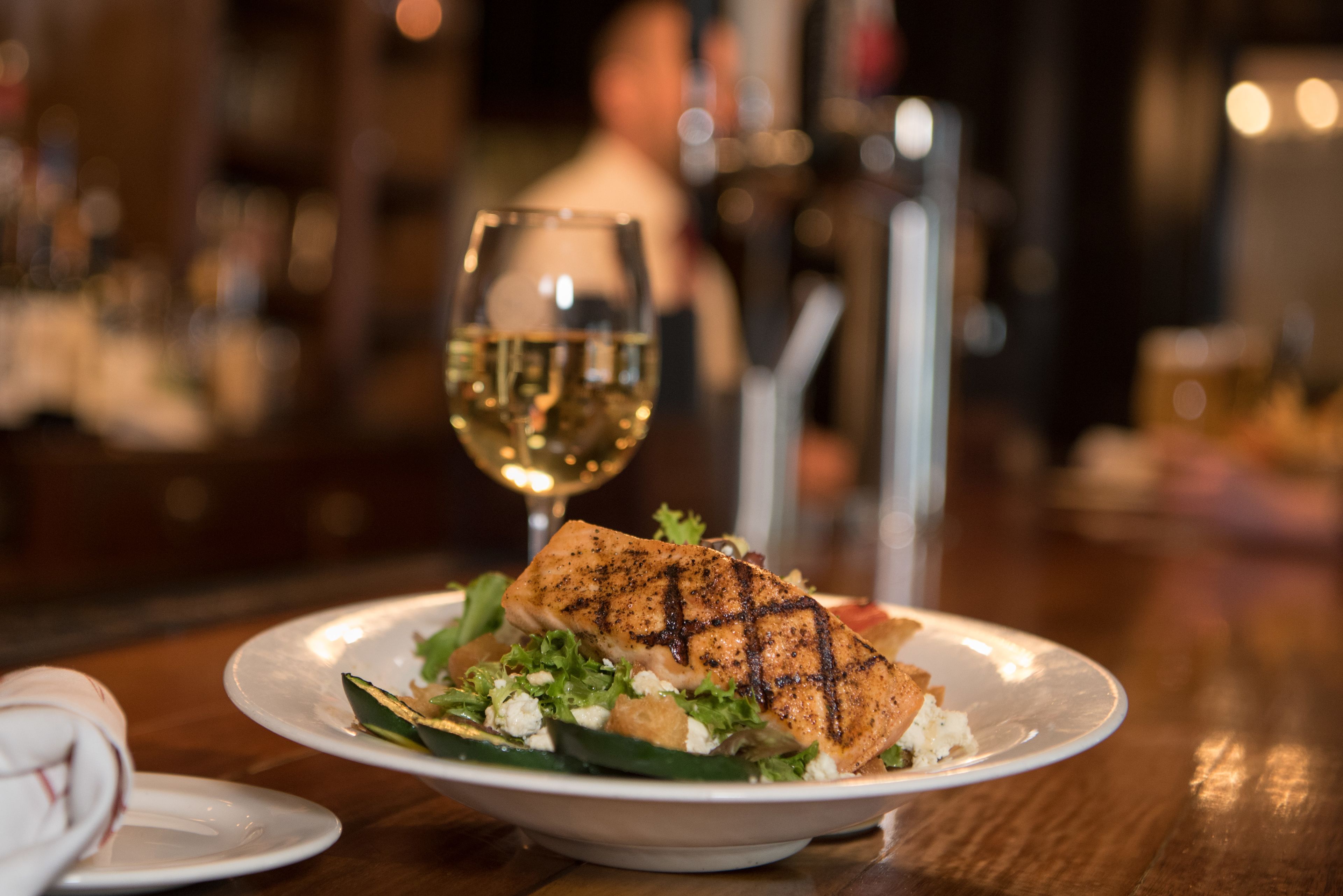 A plate of grilled salmon with a side salad and a glass of white wine on a wooden table.