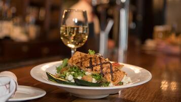 A plate of grilled salmon with a side salad and a glass of white wine on a wooden table.