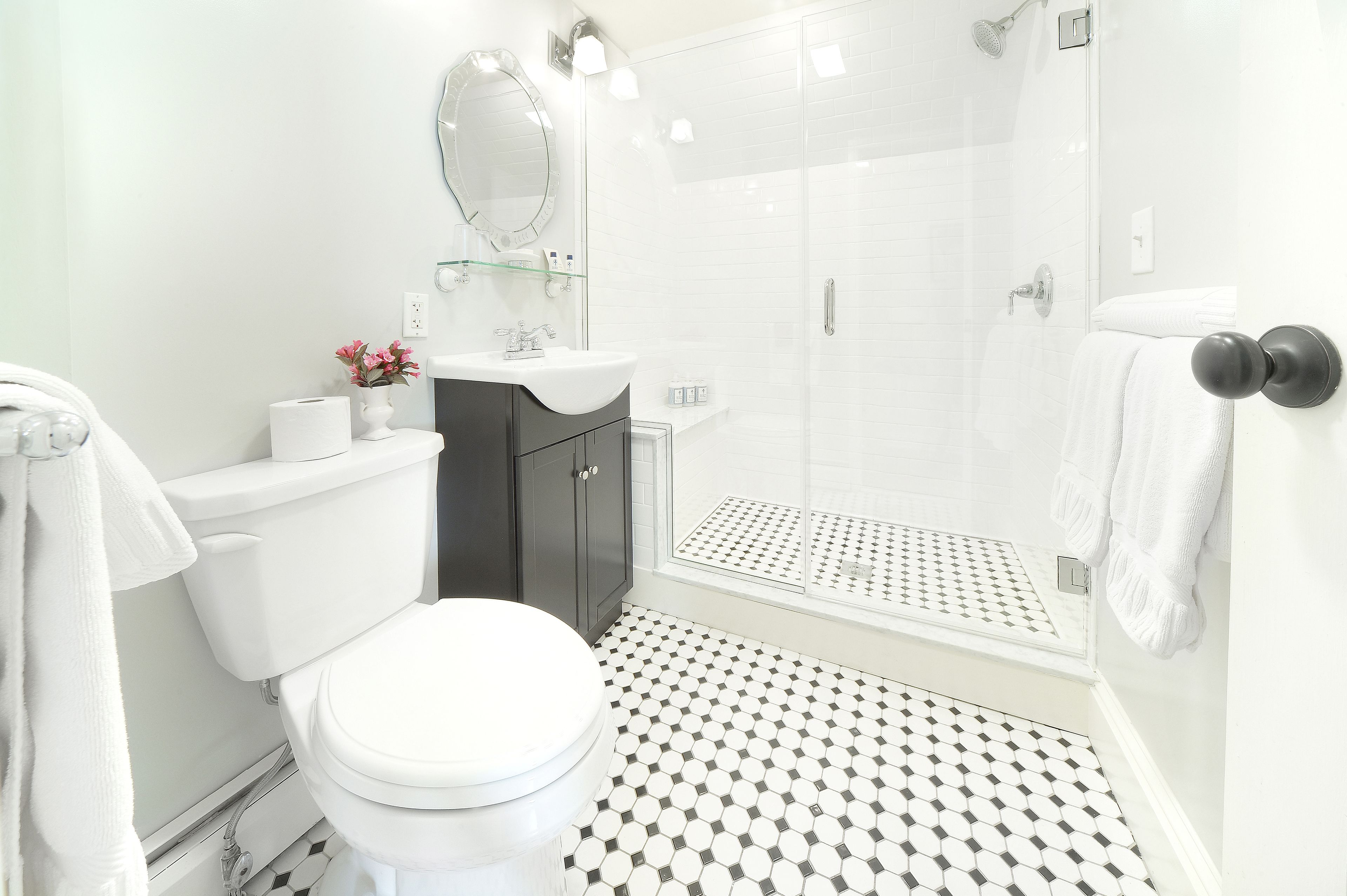 A bathroom with a toilet, sink, mirror, shower, and patterned floor.