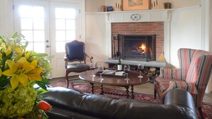 A living room with a fireplace, leather sofa, striped armchair, and a table with wine glasses. - The Springwater B&B (Saratoga Springs)