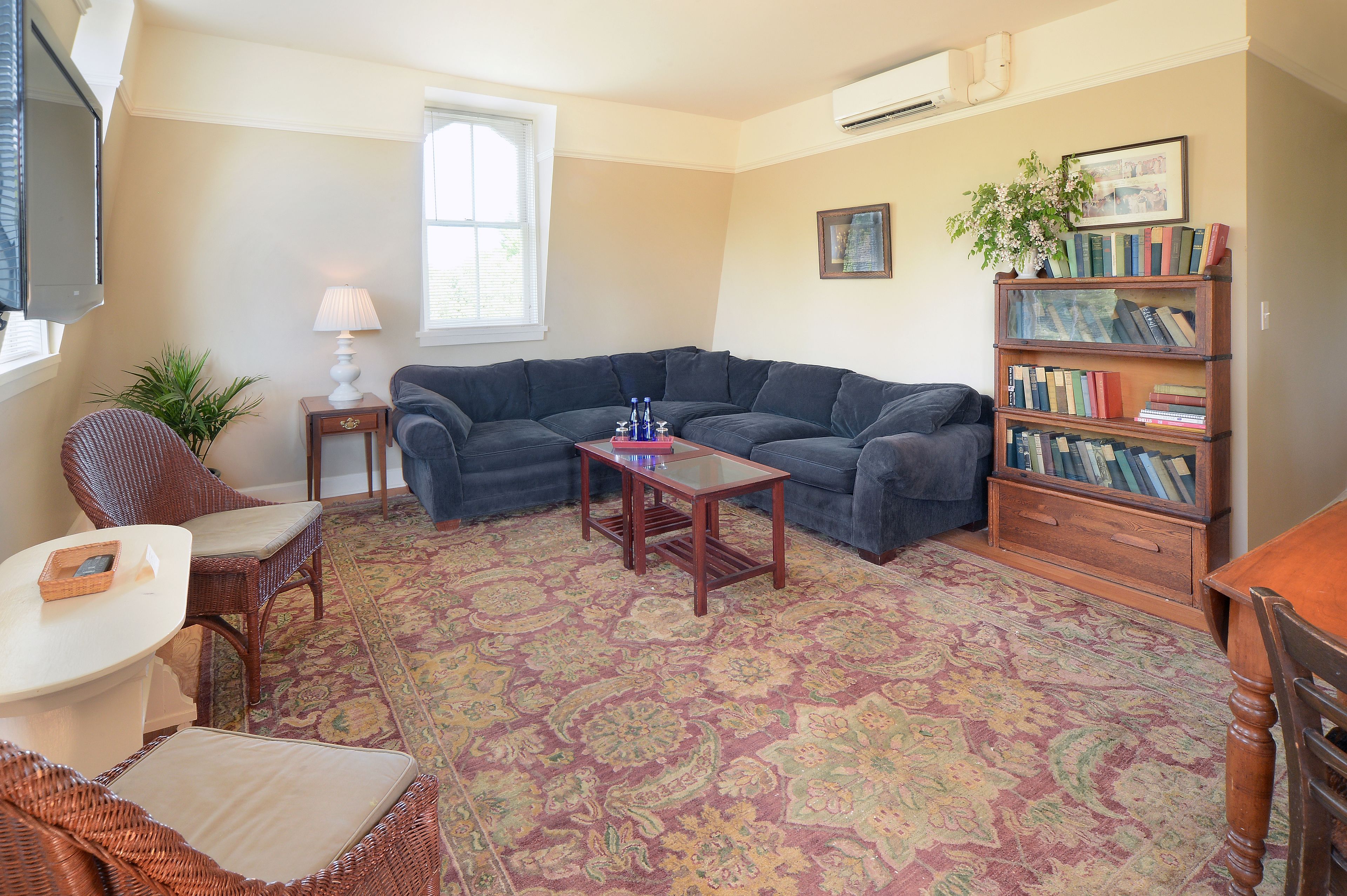 A living room with a sectional sofa, a small table, a bookshelf, and a patterned rug.