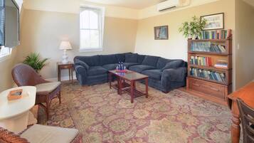 A living room with a sectional sofa, a small table, a bookshelf, and a patterned rug.