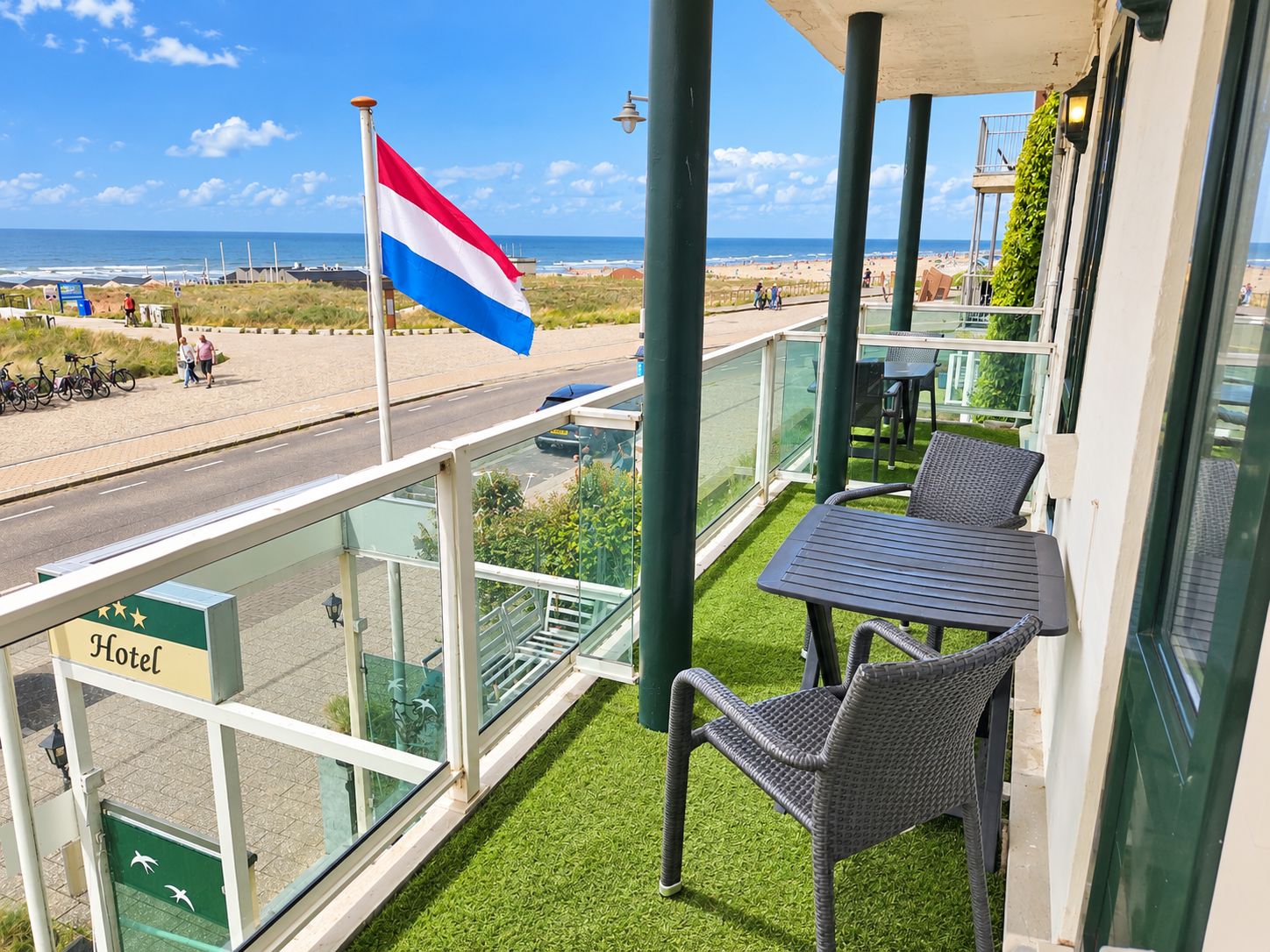 A hotel balcony with a flag, a view of the beach, and outdoor seating.