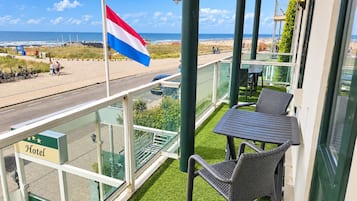 A hotel balcony with a flag, a view of the beach, and outdoor seating.