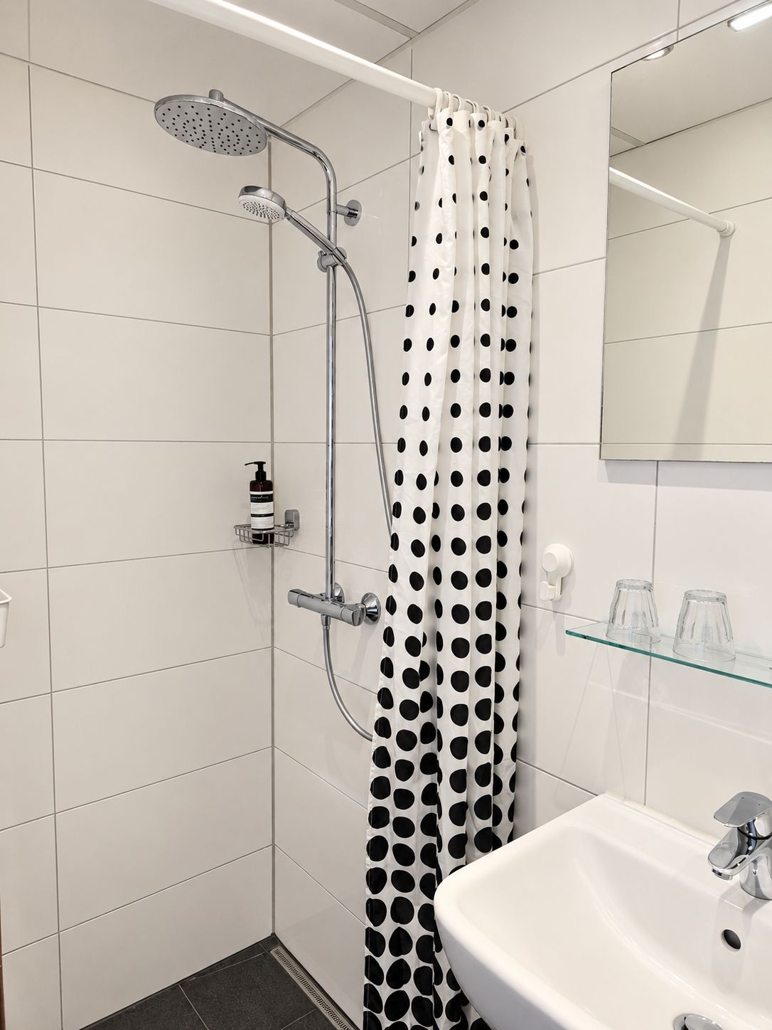 Ein modernes Badezimmer mit Dusche, einer Glasablage für Pflegeprodukte und einem weißen Waschbecken.
