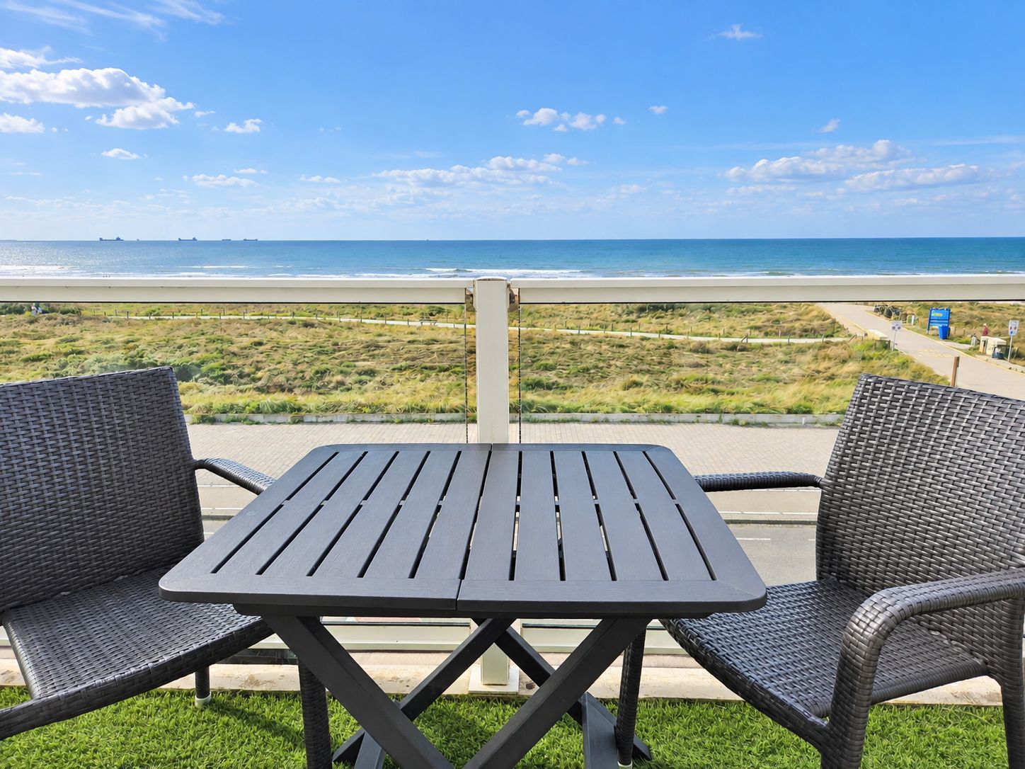 A balcony with a table and two chairs overlooking a beach.