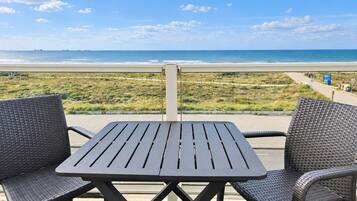 A balcony with a table and two chairs overlooking a beach.
