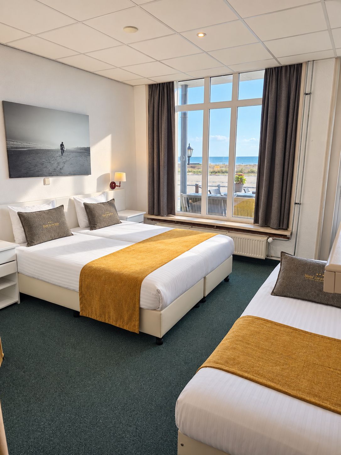 A hotel room with two beds, a large window with a view, a painting on the wall, and a nightstand with a lamp.