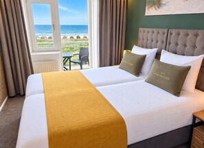 A double bed with a headboard, two pillows, a yellow throw, and a view of the beach through a window. - Hotel Zee en Duin (Katwijk Aan Zee)