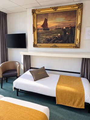 Ein Hotelzimmer mit einem Bett, einem Sessel, einem Fernseher und einem Gemälde an der Wand.