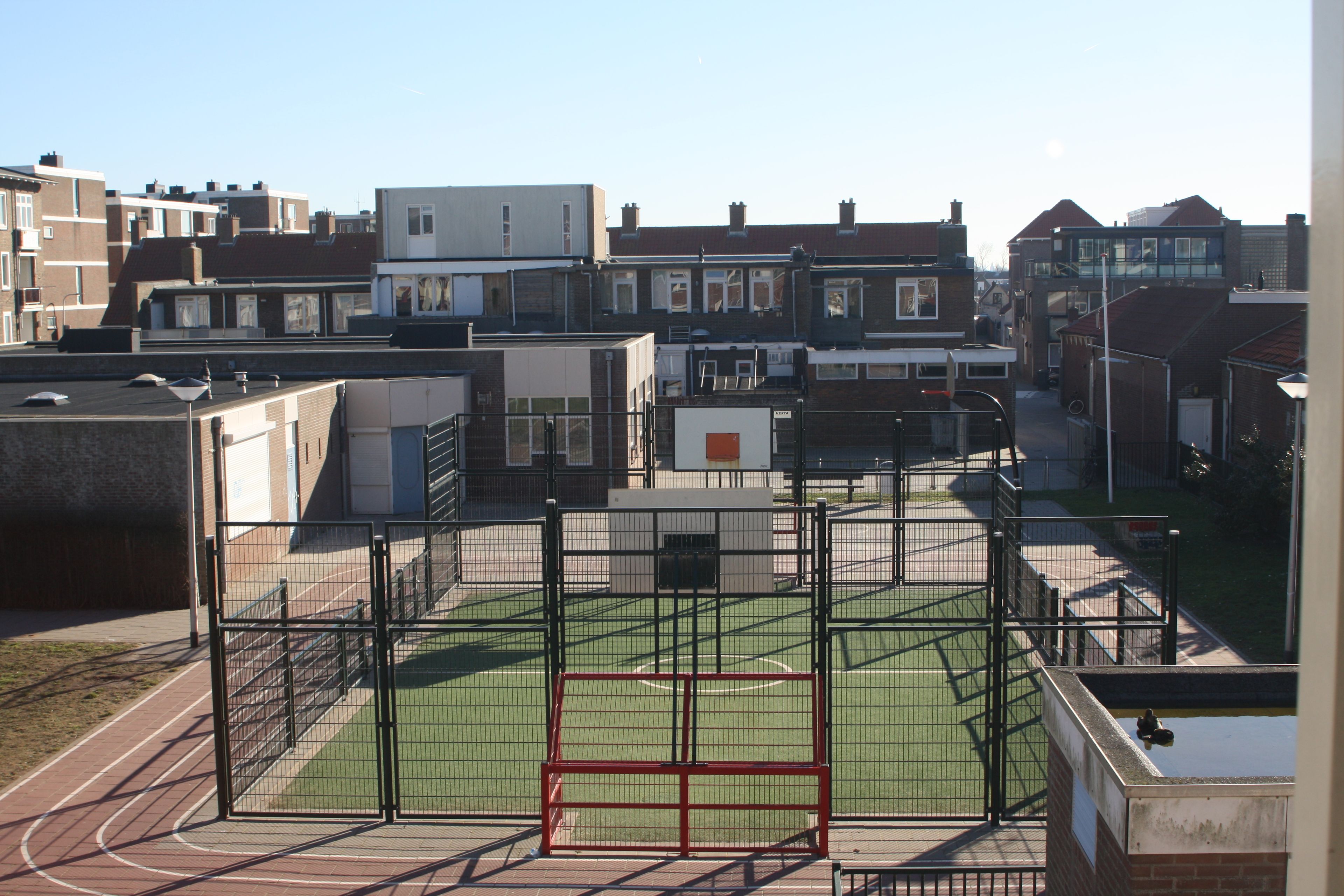 Een sportveld met een hek, omringd door woongebouwen.